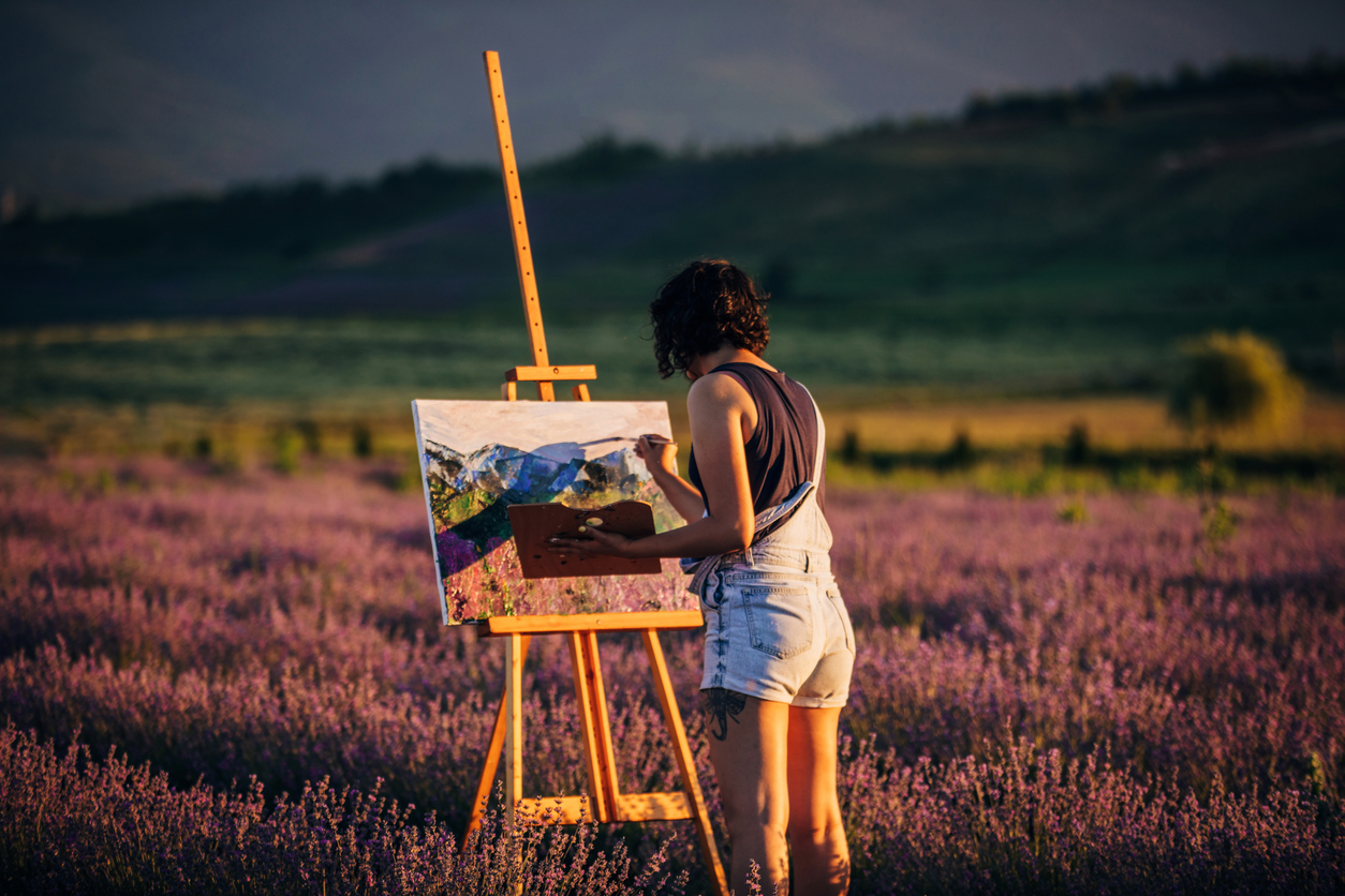 Chica pintando en mitad del campo un paisaje (© Istockphoto)